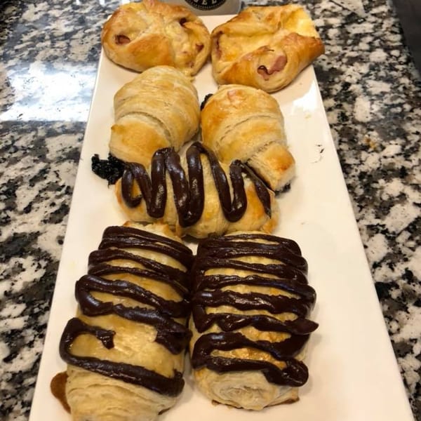 A white platter holds four pastries, two with ham and two with chocolate drizzle, on a granite counter.