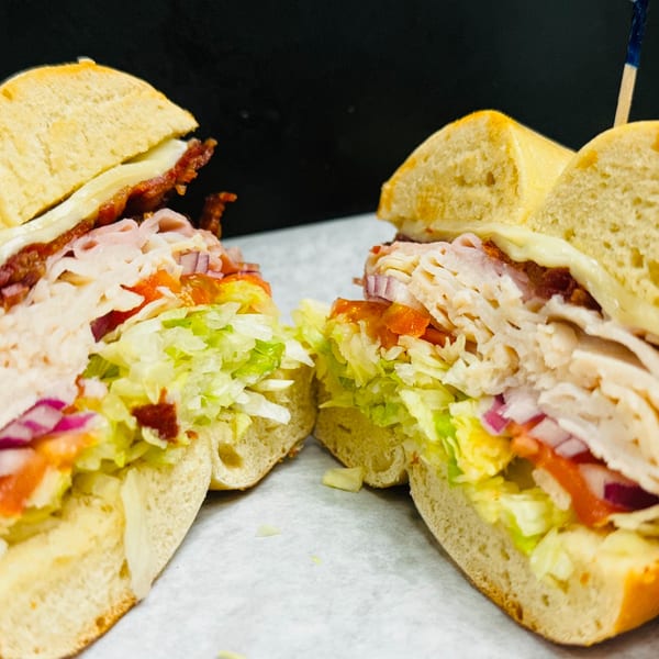 A New York Bagel Cafe bagel sandwich, cut in half, filled with turkey, bacon, cheese, lettuce, tomato, and onion.